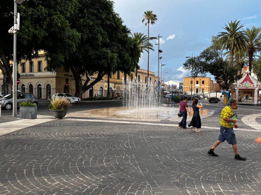 La fontana di piazza Roma — Palme, getti d'acqua e il passeggio del pomeriggio
