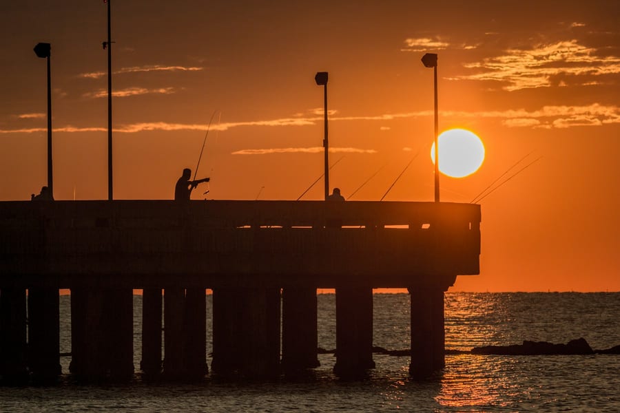 I pescatori sul pontile — Le canne da pesca controluce, all'ora in cui il sole tocca il mare